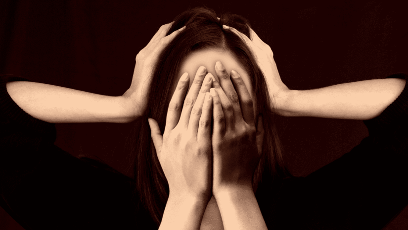 Lady with hands covering face depicting stress with someone else hands on sides of head